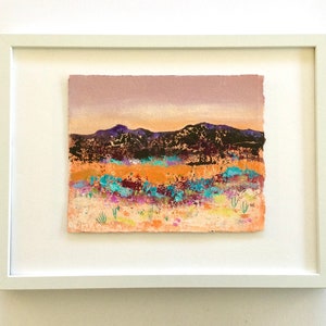 May include: A framed abstract landscape painting with a purple, orange, and blue color scheme. The painting depicts a mountain range in the background with a field of flowers in the foreground.