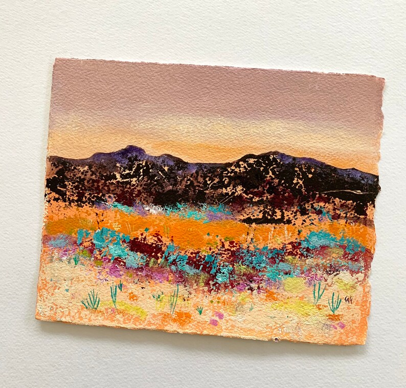 May include: A painting of a desert landscape with a purple, orange, and yellow sunset over a range of dark mountains. The foreground is a field of colorful wildflowers.