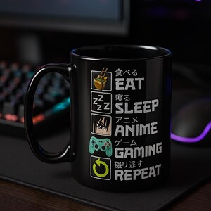 May include: Black ceramic mug with a white graphic that reads "Eat, Sleep, Anime, Gaming, Repeat" in English and Japanese. The mug features icons of food, sleeping Z's, an anime character, a game controller, and a repeat symbol.