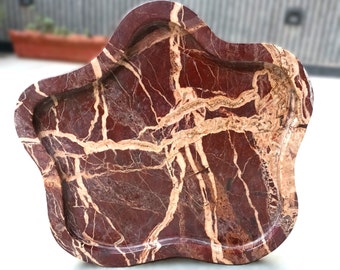 May include: A deep red marble tray with a distinct organic, cloud-like shape. The stone features prominent, branching cream-colored veins that create a high-contrast pattern across the polished, smooth surface of the decorative dish.