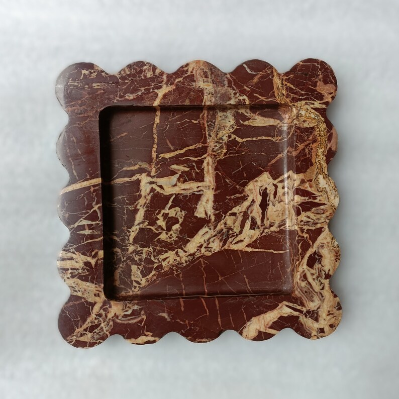 May include: A square, red and gold marble tray with a scalloped edge. The tray has a raised, square inner section.