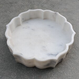 Puede incluir: Cuenco decorativo de m&aacute;rmol blanco con borde festoneado. El cuenco es redondo y tiene una superficie lisa y pulida.