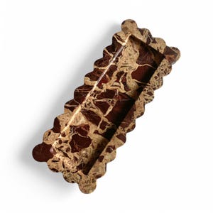 May include: A rectangular tray crafted from polished marble featuring a deep burgundy and cream-colored veined pattern. The tray has a distinct scalloped edge design along all four sides, creating a continuous wavy border around the basin.