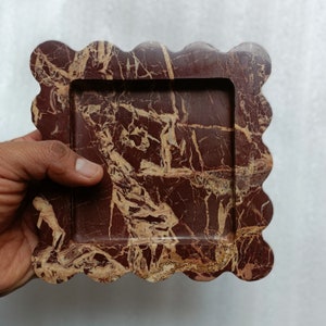 May include: A decorative tray made of red and brown marble with a scalloped edge. The tray has a rectangular inner frame.