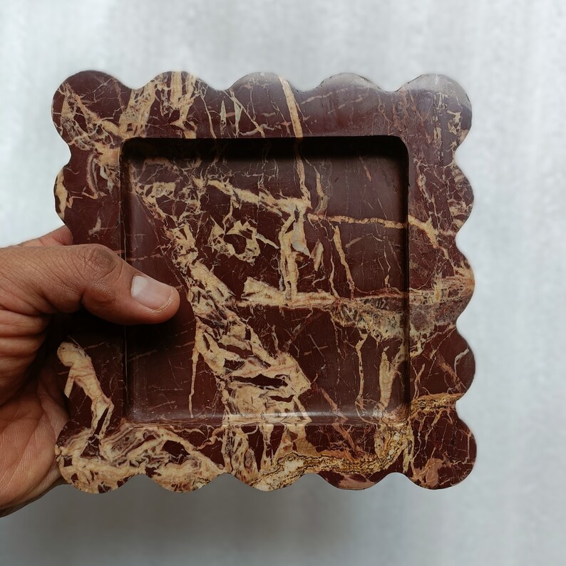 May include: A decorative tray made of red and brown marble with a scalloped edge. The tray has a rectangular inner frame.