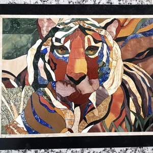 Könnte beinhalten: Eine Nahaufnahme eines Tigermosaiks aus bunten Steinen. Das Gesicht des Tigers ist der Mittelpunkt des Kunstwerks, mit seinen Streifen und Augen, die deutlich sichtbar sind. Das Mosaik ist in einen schwarzen Rahmen gefasst.
