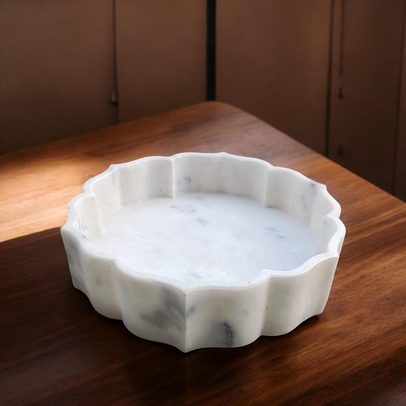 Puede incluir: Cuenco decorativo de m&aacute;rmol blanco con borde festoneado. El cuenco est&aacute; sobre una superficie de madera.