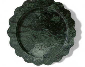 Puede incluir: Una bandeja redonda de servir de mármol verde con un borde festoneado. La bandeja es redonda y tiene una superficie lisa.