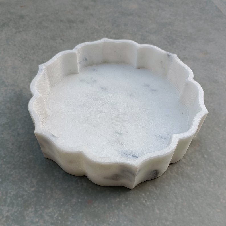 Puede incluir: Bandeja decorativa redonda de m&aacute;rmol blanco con borde festoneado. La bandeja es lisa y pulida.