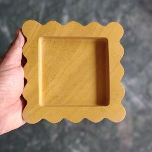 May include: A yellow square-shaped tray with a scalloped edge. The tray is made of stone and has a smooth surface.
