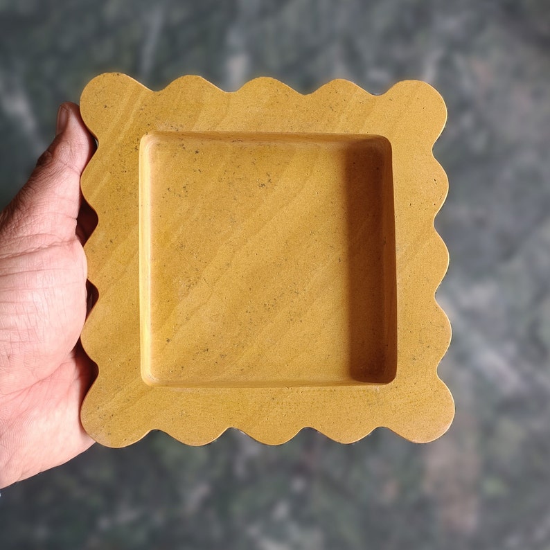 May include: A yellow square-shaped tray with a scalloped edge. The tray is made of stone and has a smooth surface.