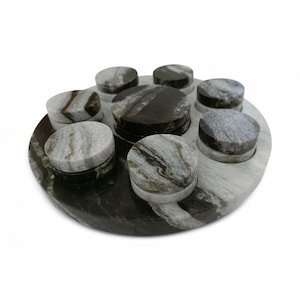 May include: A handcrafted marble game board with eight circular pieces. The board is a dark gray with lighter gray and white veining. The circular pieces are gray with dark gray and black veining. The game board is a unique decorative item.