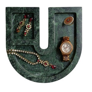 May include: A green marble U-shaped tray with three compartments. The tray holds a gold necklace with red stones, a pair of gold earrings with red stones, and a gold watch with a white face.
