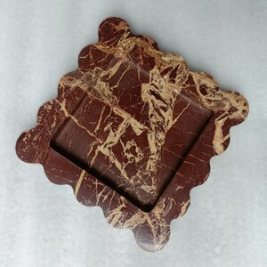 May include: A square-shaped, red and gold marble tray with a wavy edge. The tray has a square inset in the center.