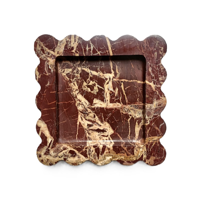 May include: A decorative tray made of red and gold marble with a scalloped edge. The tray has a rectangular shape and a smooth surface.