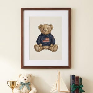 May include: A framed print of a teddy bear wearing a navy blue sweater with an American flag design. The print is in a dark brown frame. A shelf below holds a teddy bear, a trophy, a sailboat, and books.