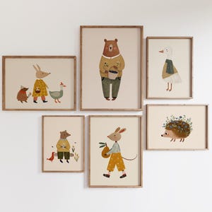 Puede incluir: Colección de seis láminas artísticas enmarcadas con ilustraciones caprichosas de animales del bosque. La obra de arte incluye un oso, un conejo, un ganso, un erizo y un ratón, todos representados en un estilo encantador con colores suaves y atuendos detallados.