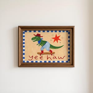 A framed painting depicting a dinosaur riding a skateboard, with the text "yeehaw" written below the dinosaur.