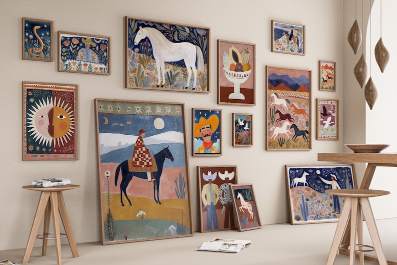 Op de afbeelding: Een verzameling ingelijste kunstprints met een thema uit het zuidwesten. De kunstwerken tonen illustraties van paarden, cowboys en woestijnlandschappen in een kleurrijke, folk art-stijl. De prints worden tentoongesteld op een neutrale muur met houten krukken.