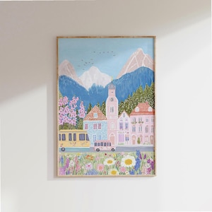 Può includere: Una stampa artistica incorniciata raffigurante una pittoresca scena di un villaggio europeo. L'opera presenta un autobus giallo, un autobus rosa ed edifici colorati sullo sfondo di montagne e cielo blu. Un campo di fiori selvatici è in primo piano.
