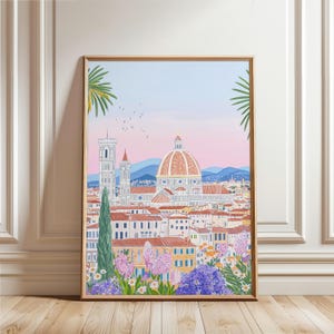 Puede incluir: Una impresión artística enmarcada que representa una colorida ilustración de Florencia, Italia. La obra presenta el Duomo, otros edificios y un primer plano floral. El cielo transita del rosa al azul, y la impresión está en un marco dorado.