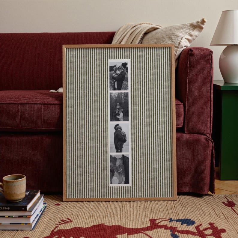 May include: A framed photo display with a wooden frame and a green and white striped fabric background. The display holds four black and white photographs. The frame is leaning against a burgundy sofa.