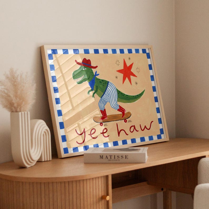 a framed artwork depicting a dinosaur riding a skateboard, with the text "Yeehaw" written below the dinosaur.