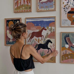 Op de afbeelding: Een verzameling ingelijste kunstprints met kleurrijke illustraties. E&eacute;n print toont een rood en zwart paard dat door een woestijnlandschap rent. Andere prints tonen verschillende dieren en natuursc&egrave;nes, allemaal in houten frames.