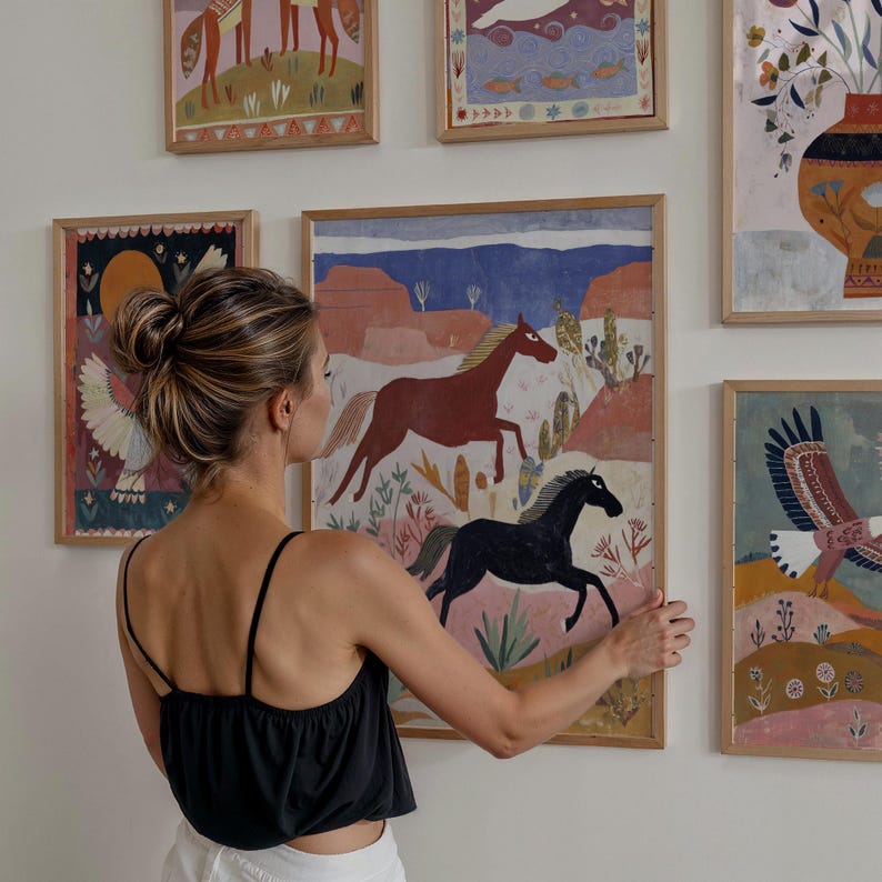 Op de afbeelding: Een verzameling ingelijste kunstprints met kleurrijke illustraties. E&eacute;n print toont een rood en zwart paard dat door een woestijnlandschap rent. Andere prints tonen verschillende dieren en natuursc&egrave;nes, allemaal in houten frames.