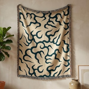 Puede incluir: Una manta beige con un patrón abstracto de líneas curvas en color verde oscuro. La manta tiene un borde con flecos y está colgada en una pared. El diseño es moderno y complementaría una variedad de estilos de decoración del hogar.
