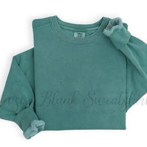 May include: A teal-colored sweatshirt with a crew neck and long sleeves. The cuffs and collar have a slightly faded, textured appearance. The words "Unisex Blank Sweatshirt" are faintly visible across the front.