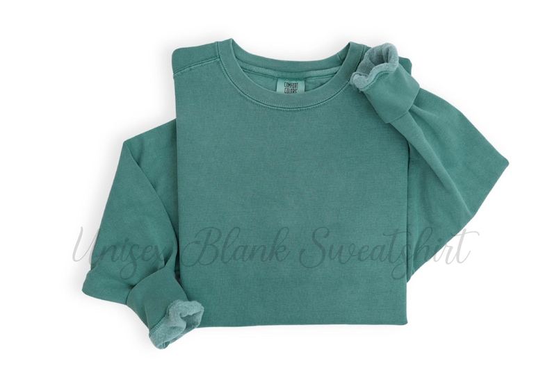 May include: A teal-colored sweatshirt with a crew neck and long sleeves. The cuffs and collar have a slightly faded, textured appearance. The words "Unisex Blank Sweatshirt" are faintly visible across the front.