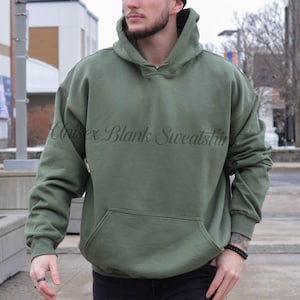 May include: Olive green hooded sweatshirt with a front pocket. The text "Unisex Blank Sweatshirt" is printed on the front. The sweatshirt is made of a soft material and has long sleeves.