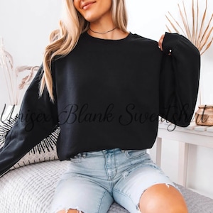 May include: A black unisex sweatshirt with long sleeves. The text "Unisex Blank Sweatshirt" is printed on the front. The model is wearing light blue denim shorts.