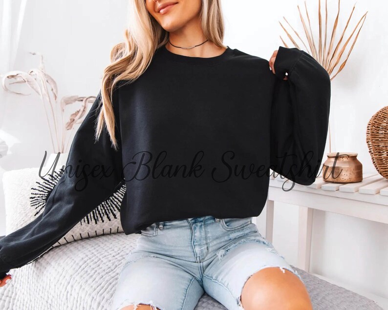 May include: A black unisex sweatshirt with long sleeves. The text "Unisex Blank Sweatshirt" is printed on the front. The model is wearing light blue denim shorts.