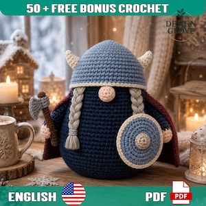 May include: A crochet gnome doll wearing a blue Viking helmet with horns, a dark blue tunic, and a maroon cape. The gnome has two braided blonde pigtails, a round nose, and holds a small grey axe in one hand and a round blue shield in the other.