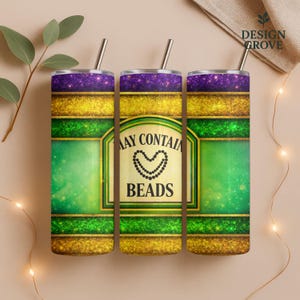 May include: Three stainless steel tumblers with straws, featuring a purple glitter top, gold glitter band, and green center. The center label reads "MAY CONTAIN BEADS" with a beaded heart design. The tumblers are designed with a Mardi Gras theme.