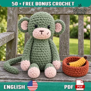 Puede incluir: Un peluche de mono tejido a ganchillo en color verde salvia con detalles en rosa claro en las orejas, manos y pies, con ojos de seguridad negros y boca bordada. Junto al mono hay una pequeña cesta tejida de color óxido con un plátano amarillo.