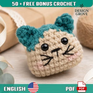 May include: A small, handmade crochet cat head amigurumi featuring teal ears and a beige face. It has two round black plastic eyes, a stitched black nose and whiskers, and light pink blush accents on the cheeks. The text 50 + FREE BONUS CROCHET and DESIGN GROVE are visible.
