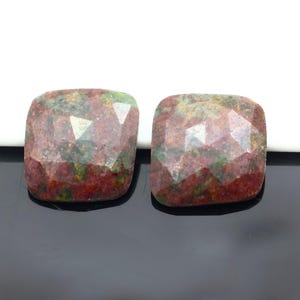 Può includere: Due pietre preziose quadrate e sfaccettate. Le pietre presentano un mix di colori rosso, verde e marrone. Le sfaccettature creano un effetto scintillante. Le pietre sono poste su uno sfondo bianco e nero.