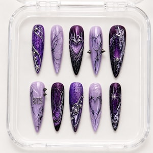 Pode incluir: Um conjunto de dez unhas postiças em formato stiletto em tons de roxo e violeta escuro. Os designs apresentam detalhes metálicos prateados, motivos de coração em relevo, texturas, pequenos tachas prateadas e as letras BTS em prata.
