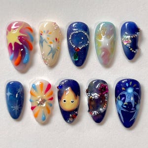 May include: A set of ten artificial nails with various designs. The nails feature colorful abstract art, celestial patterns, and character illustrations. Designs include a sunburst, stars, and a cartoon character. Each nail has a glossy finish.