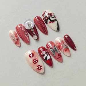 May include: A set of artificial nails in diverse designs. The nails showcase red, white, and pink tones. Some nails have intricate patterns, including floral designs, geometric shapes, and silver accents. One nail has the text "방탄소년단" in Korean.
