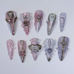 May include: A collection of ten artificial nails in various designs. The nails feature a palette of pink, white, and gold, with intricate embellishments including hearts, stars, and geometric shapes. Each nail has a unique design, showcasing a variety of textures and finishes.