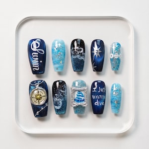 May include: A set of ten artificial nails with various designs. The nails feature shades of blue, with designs including stars, compasses, and the words "Swim" and "Just Wanna Dive". Some nails have a glittery finish.