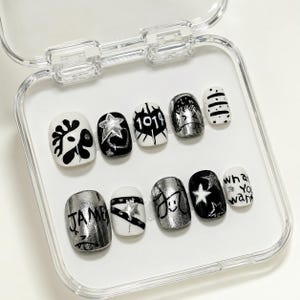 May include: A set of ten press-on nails in a clear plastic case, featuring a black, white, and metallic silver color palette. The designs include hand-drawn stars, hearts, the text 1014, JAMES, and what you want, along with various abstract patterns.