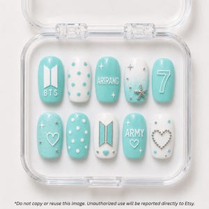 May include: A set of ten press-on nails in a clear plastic case, featuring a teal and white color palette. Designs include the BTS logo, the number 7, the text ARIRANG and ARMY, polka dots, a starfish, silver studs, and heart shapes.