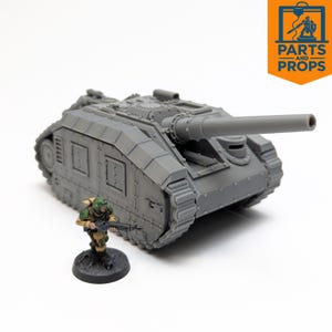 Puede incluir: Un modelo gris impreso en 3D de un tanque con un cañón largo, orugas y paneles laterales rectangulares. Una figura de soldado en miniatura con uniforme de camuflaje está de pie frente al tanque. El texto "PARTS AND PROPS" está en un cuadro naranja.