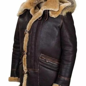 Peut inclure: Veste en cuir marron foncé avec capuche et bordure en fourrure. La veste est dotée d'une poche zippée, de fermetures à bascule et d'une doublure en peau de mouton chaude. Manteau d'hiver.