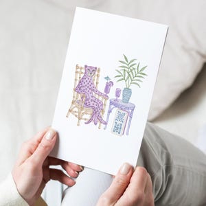 K&ouml;nnte beinhalten: Eine wei&szlig;e Gru&szlig;karte mit einer farbenfrohen Illustration eines lila gefleckten Leoparden, der auf einem beigen Bambusstuhl sitzt. Der Leopard h&auml;lt einen lila Cocktail mit einem blauen Schirmchen. Daneben steht ein kleiner Tisch mit einer Pflanze.